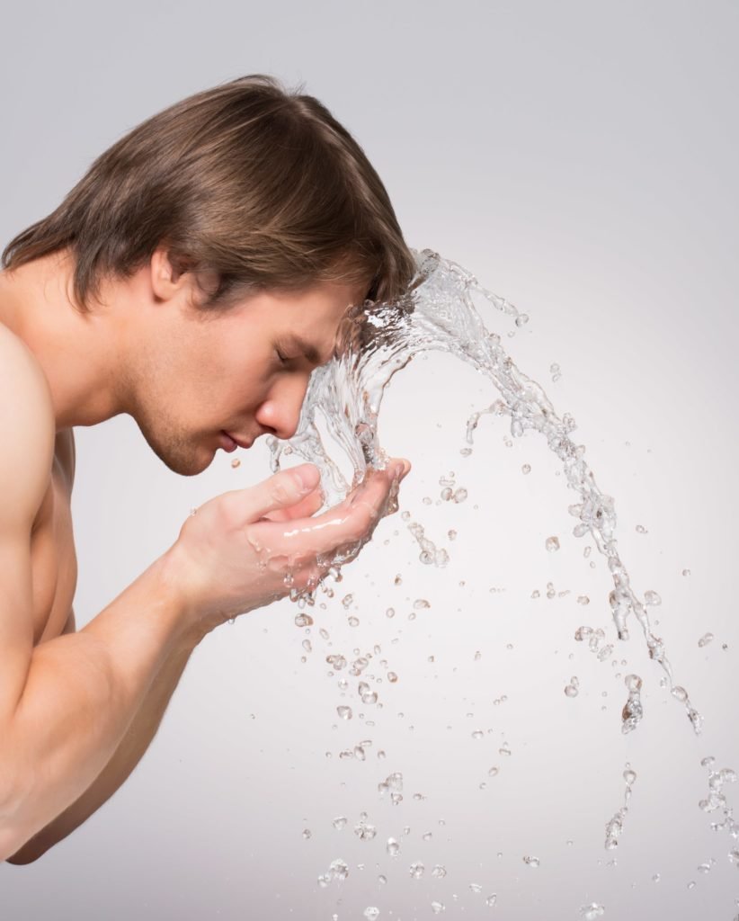 profile portrait of handsome man washing his face with water on gray wall min scaled